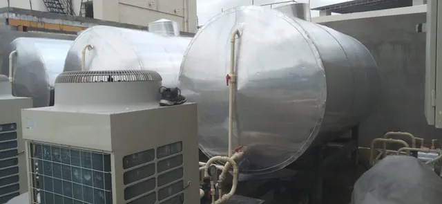 Several insulated hot water tanks with heat pump units in a plant area