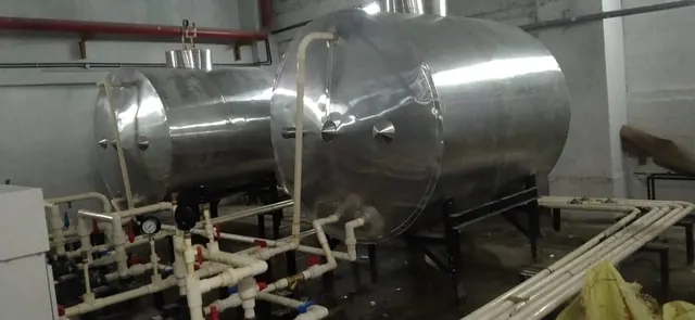 Two insulated hot water tanks with pipework in a plant room